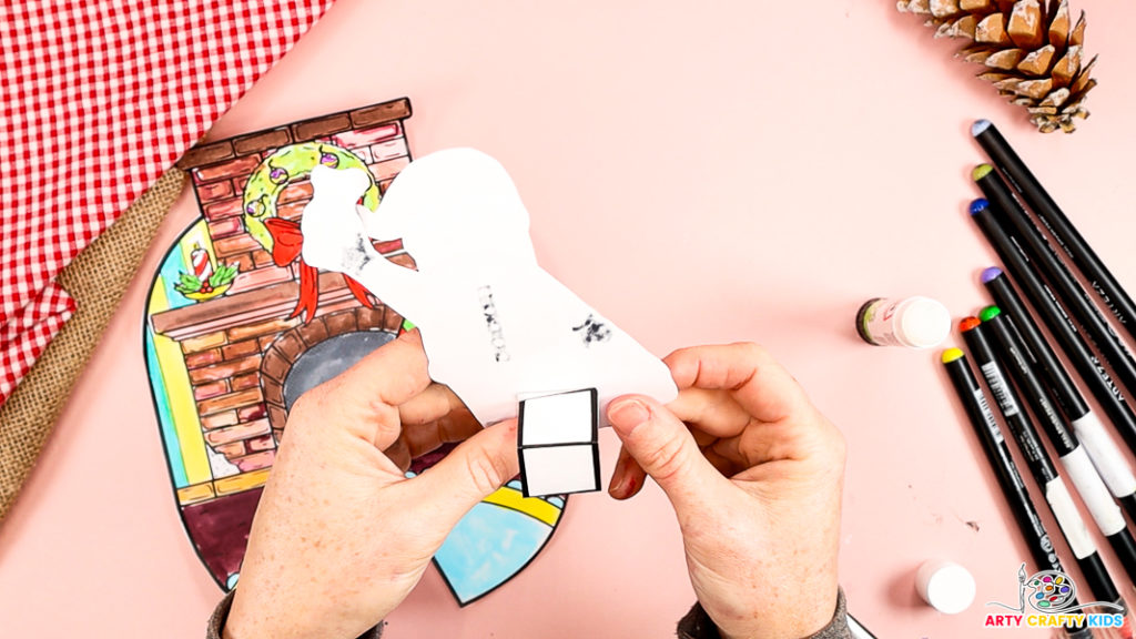 Image features a hand affixing the paper cube behind Santa.