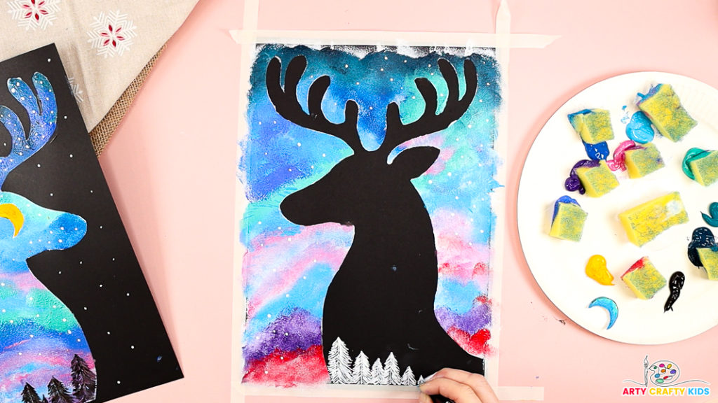 Image of a hand drawing white trees within the black reindeer silhouette.