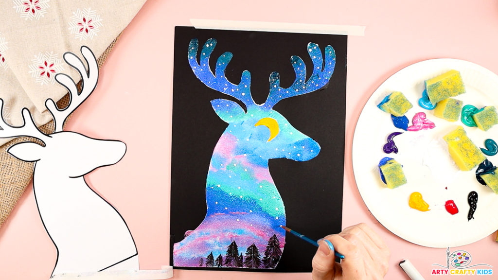 Image features a hand painting white spots within the reindeer painting.