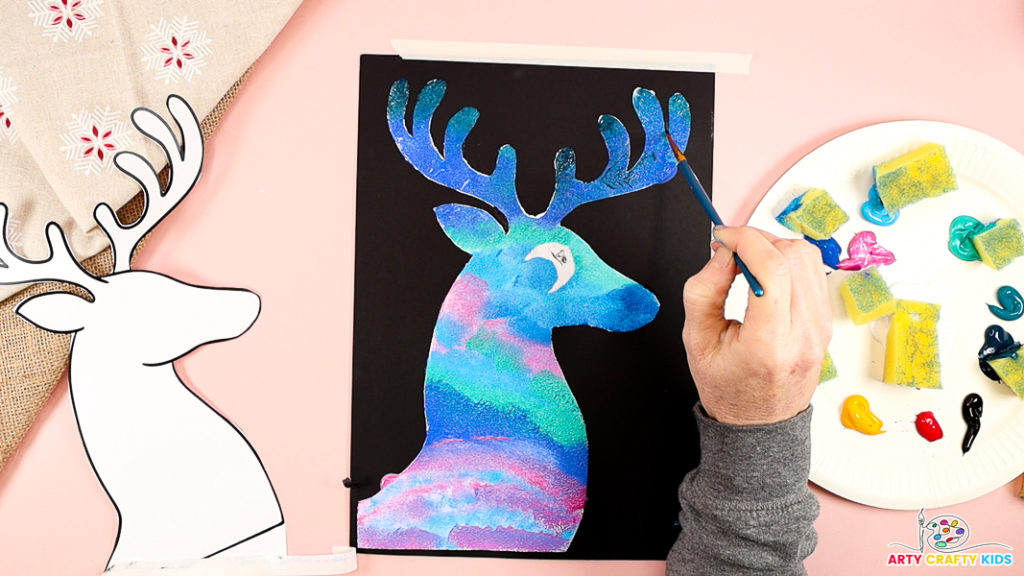 Image features a hand tidying up the reindeer outline with black paint.