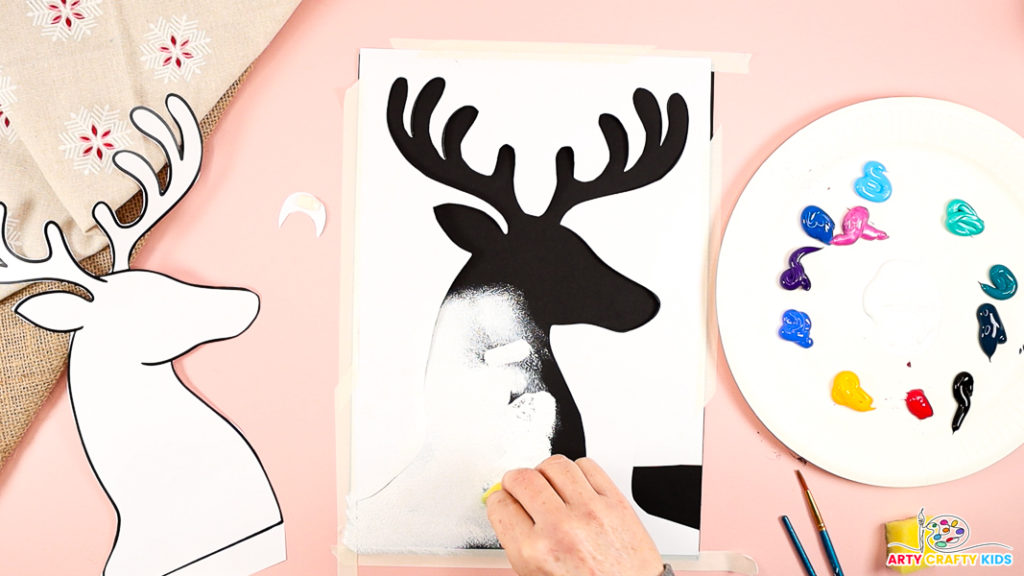 The image features a hand dabbing white paint within the reindeer silhouette.