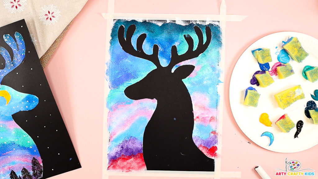 Image features a black reindeer silhouette contrasting with the colorful sky background.