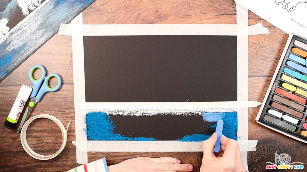 Image featuring a hand using a blue chalk pastel to fill the black space below the masking tape line.