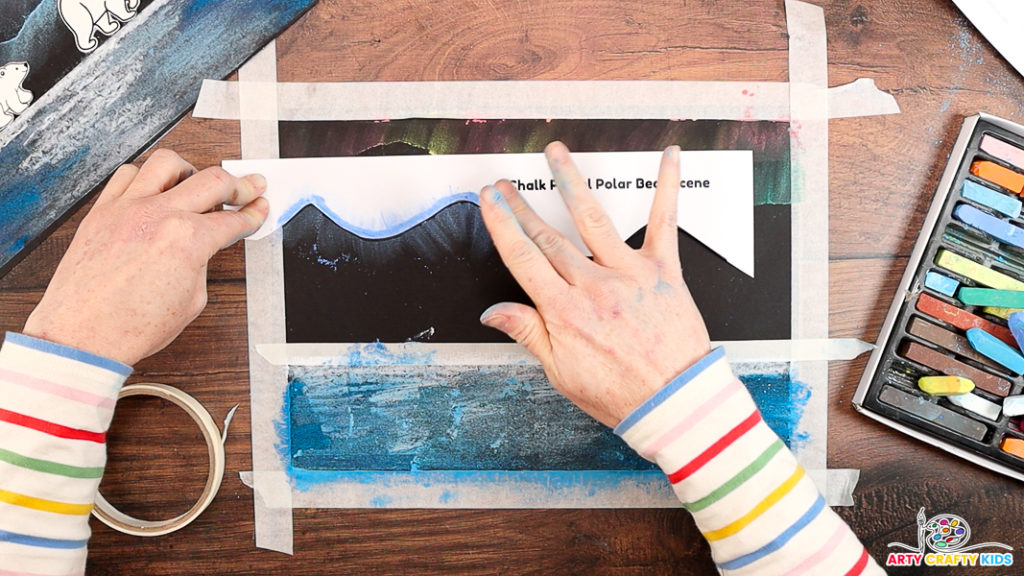 Image of a hand blending the blue chalk pastels to create mountains.