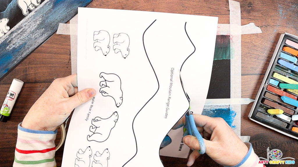 Image featuring a hand cutting out the mountain lines from the polar bear template.