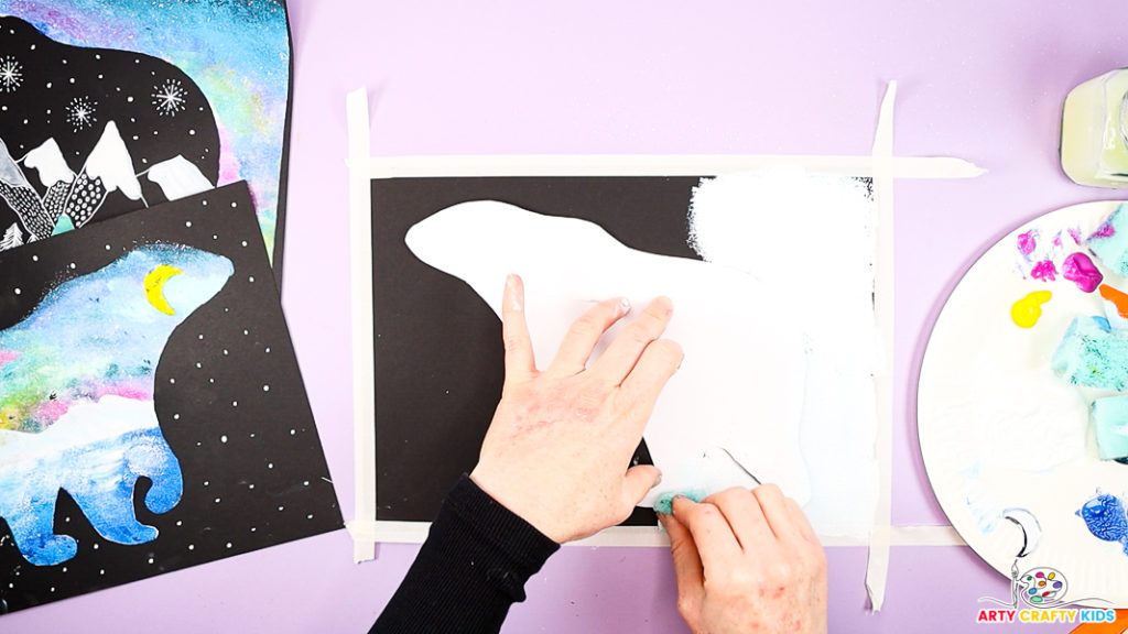 Image of a hand sponge painting the area around the polar bear white.