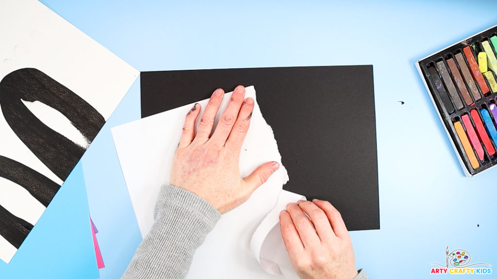 Image of a hand tearing white paper to create a jagged edge in preparation for creating the northern lights with chalk pastels.