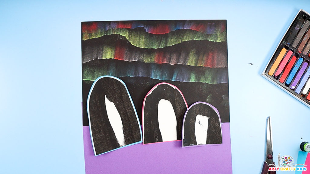 Image showing three cut out scrape painted penguins onto blue, pink and purple backing paper.