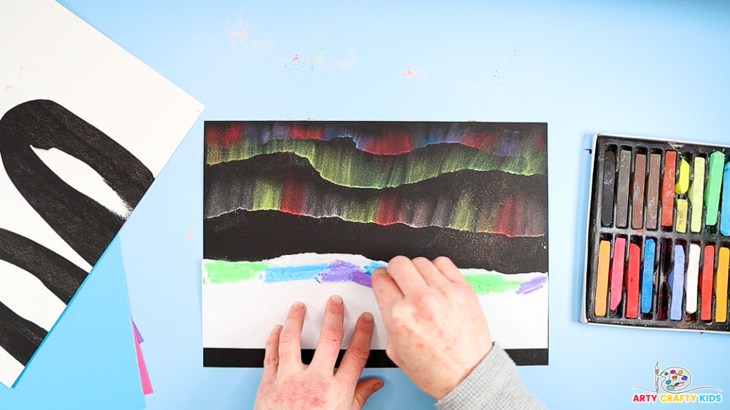 Image showing three rows of Northern lights in varying colors. A hand is applying green, blue, and purple chalk to a jagged paper edge.