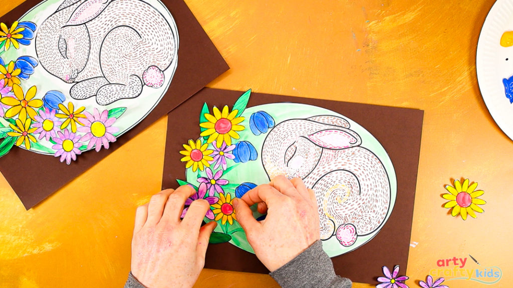 Image of a hand glueing the remaining flowers around the bunny.