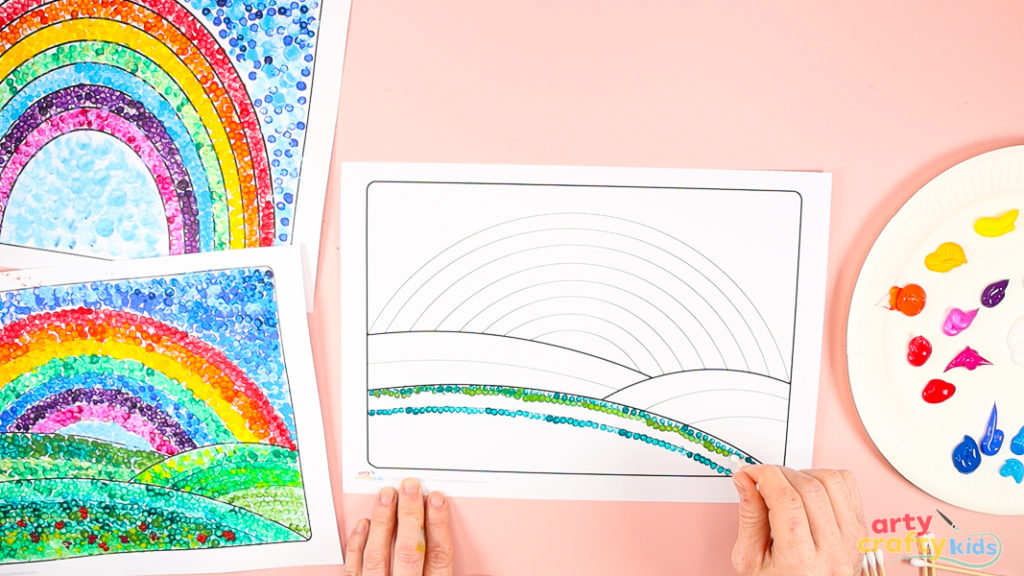 The image shows a hand using a Q-tip to create the first rows of green dots, gradually filling the hill.