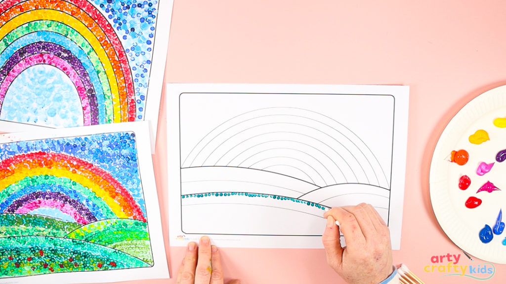 Image of a hand using a q-tip to paint a row of dots in the first hill of the landscape and rainbow art template.